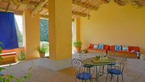 Un patio techado con una mesa redonda, sillas y un sofá con cojines.