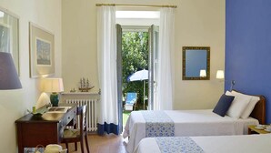 Habitación de hotel con dos camas, un escritorio con lámpara, un modelo de barco pequeño y vistas al exterior.