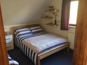 A bedroom with a wooden bed, striped bedding, a nightstand, a dresser, and a window with a curtain.