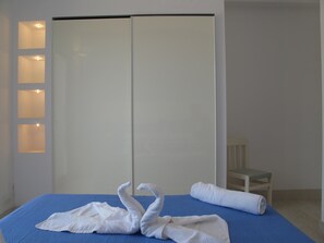 A hotel room with a bed, a blue mattress, a white towel, and a white chair.