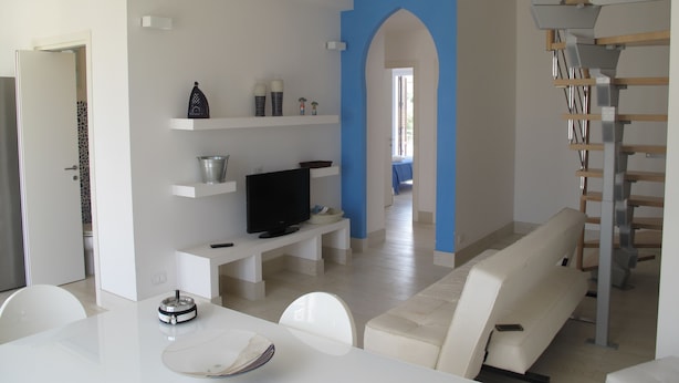 Un moderno salón con televisor, muebles blancos y una pared de acento azul.