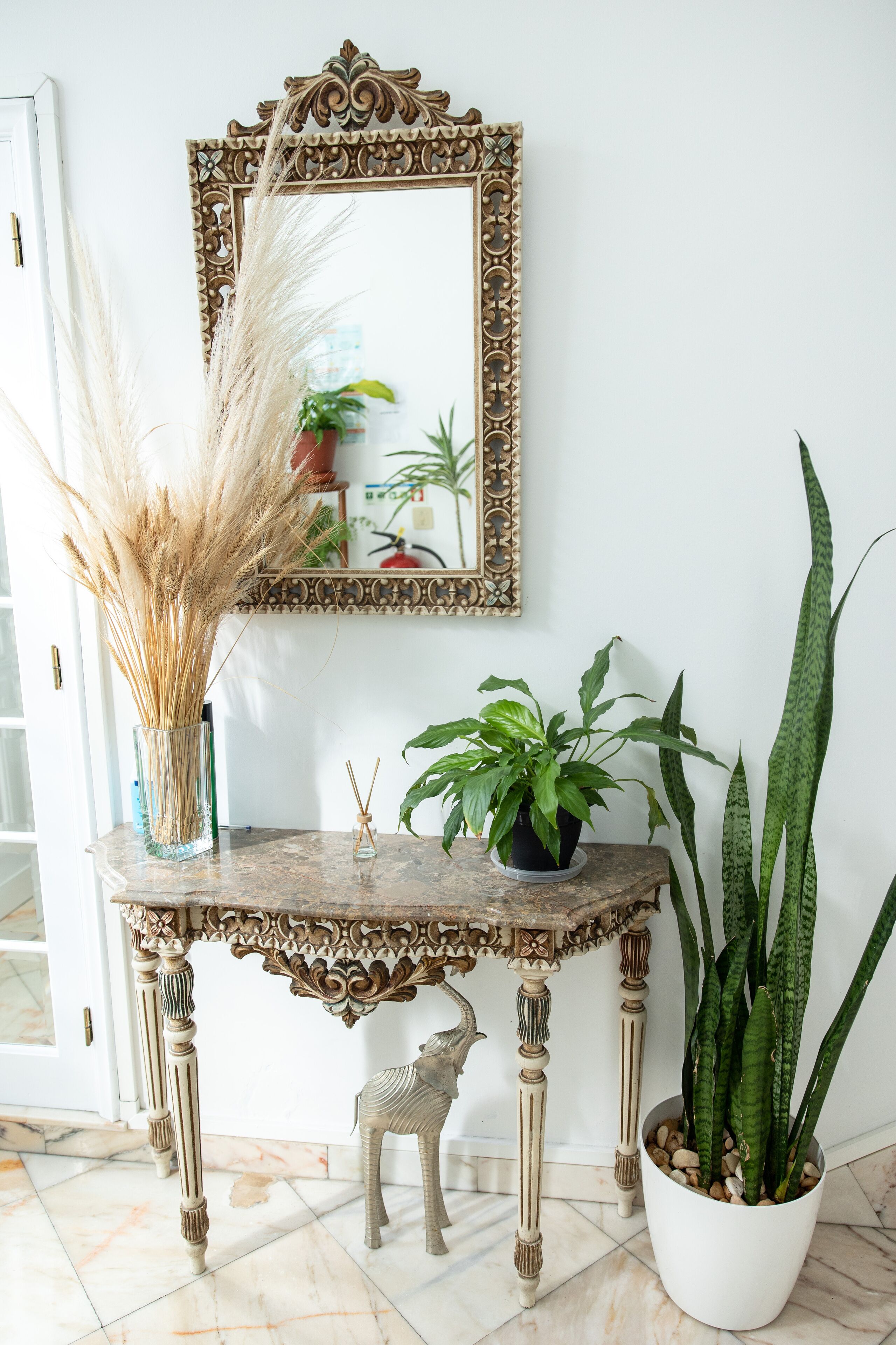 A decorative console table with a mirror, a vase with pampas grass, and potted plants.
