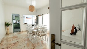 A dining area with a white table and chairs, a hanging light fixture, and a view into the kitchen. - TMO Residence 2 P. D.L (Ponta Delgada)