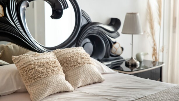 A neatly made bed with two textured pillows, a large ornate mirror, and a bedside table with a lamp and a small vase. - TMO Residence 2 P. D.L (Ponta Delgada)