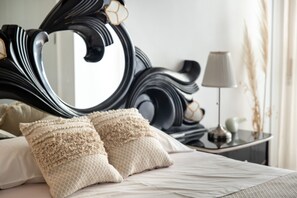 A neatly made bed with two textured pillows, a large ornate mirror, and a bedside table with a lamp and a small vase. - TMO Residence 2 P. D.L (Ponta Delgada)