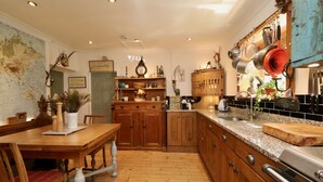 A kitchen with wooden cabinets, a granite countertop, and a dining table with chairs. - Unique 18th Century village cottage near Loch Lomond and Trossachs/ shop and pub (Killearn)