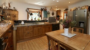 A kitchen with wooden cabinets, a granite countertop, and a stainless steel refrigerator. - Unique 18th Century village cottage near Loch Lomond and Trossachs/ shop and pub (Killearn)