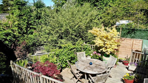 A wooden deck with a round table and chairs, surrounded by potted plants and a wooden fence. - Unique 18th Century village cottage near Loch Lomond and Trossachs/ shop and pub (Killearn)