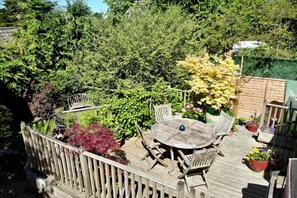 A wooden deck with a round table and chairs, surrounded by potted plants and a wooden fence. - Unique 18th Century village cottage near Loch Lomond and Trossachs/ shop and pub (Killearn)