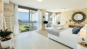 A modern bedroom with a large bed, a bathroom with a bathtub, and a view of the sea. - Majestic Sea and Sunset view, private heated pool, Luxury villa (Kalathas)