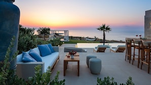 A terrace with a view of the sea at sunset, featuring a sofa, dining table, and lounge chairs. - Majestic Sea and Sunset view, private heated pool, Luxury villa (Kalathas)