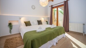 A bedroom with a bed, green bedspread, white pillows, a hanging light fixture, a window with curtains, and a plant on the wall. - SA PUNTA - Villa with private pool in Son Carrio. Free WiFi (Sant Llorenç des Cardassar)