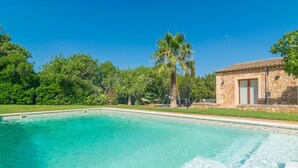 A swimming pool with clear blue water, surrounded by lush greenery and a stone building with a tiled roof. - SA PUNTA - Villa with private pool in Son Carrio. Free WiFi (Sant Llorenç des Cardassar)