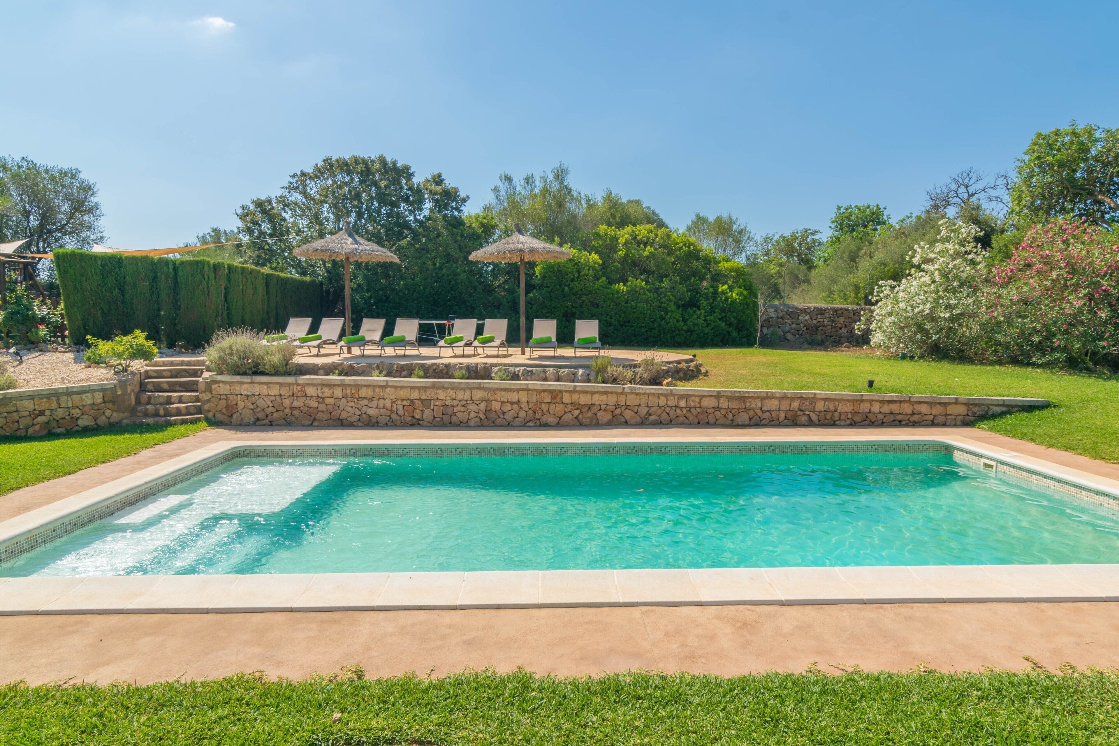 A rectangular swimming pool with a stone border, surrounded by a grassy area and a stone wall.