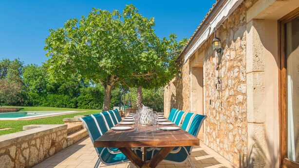 An outdoor dining area with a wooden table and blue chairs, surrounded by stone walls and a pool. - SA PUNTA - Villa with private pool in Son Carrio. Free WiFi (Sant Llorenç des Cardassar)