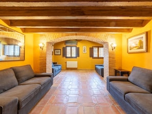 Um interior aconchegante com piso de pedra, dois sofás, lareira e teto de madeira.