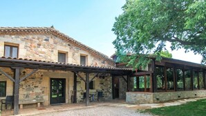 A stone building with a covered patio area, outdoor seating, and a gravel driveway.