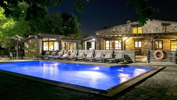 A swimming pool with lounge chairs and a stone building with windows.
