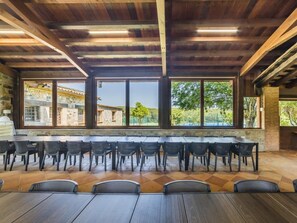 Een ruime kamer met een hoge plafond, grote ramen en uitzicht op een stenen gebouw en groen buiten.