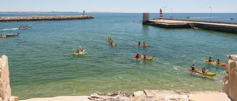 A coastal scene with kayakers on the water, a lighthouse, and a stone pier.
