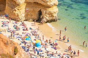 A crowded beach with people sunbathing and swimming, a large rock formation, and clear blue water. - Beachfront modern apartment [55] (Lagos)