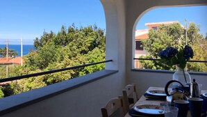A dining area with a table set for two, overlooking a scenic view of the sea and greenery.
