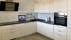 A modern kitchen with white cabinets, a black countertop, a built-in oven, and a hanging light fixture.