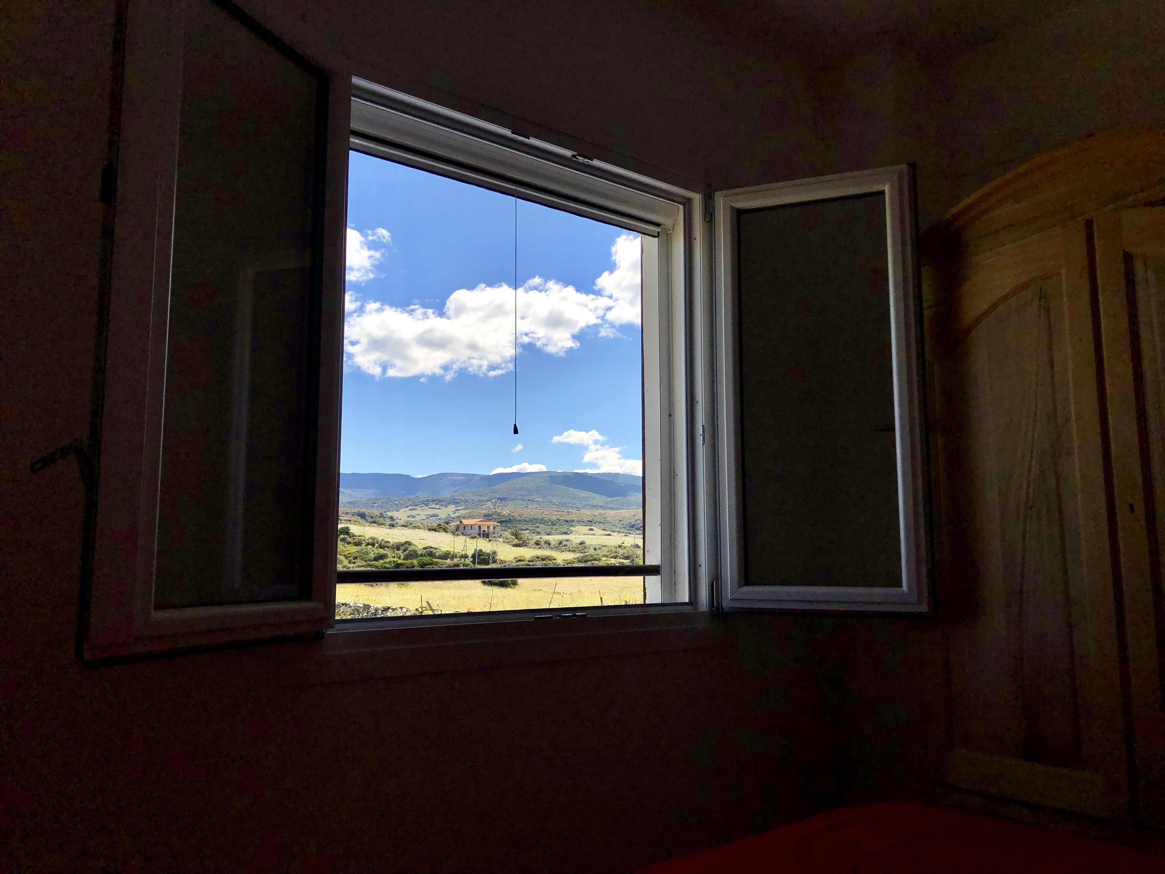 A room with a window offering a view of a landscape with hills and a building.