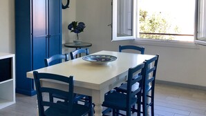 A dining area with a white table, blue chairs, a blue cabinet, and a window with a view of greenery.
