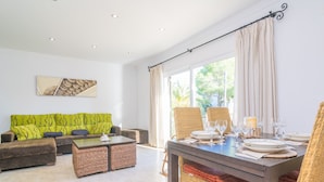 A spacious living area with a sofa, coffee table, and dining table set up for a meal. - LLUNA HOME - Chalet with terrace in Colonia de Sant Jordi. Free WiFi (Ses Salines)