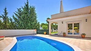 Una piscina con bordo piastrellato, un patio coperto e un edificio con facciata bianca e tetto a cono.