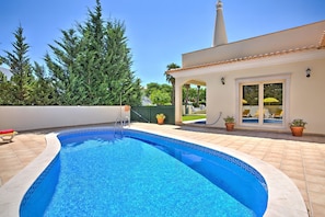 A swimming pool with a tiled edge, a covered patio area, and a building with a white exterior and a conical roof. - Villa w/ Heatable Pool & BBQ in Albufeira (Albufeira)