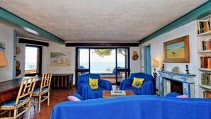 Ein Zimmer mit Meerblick, ausgestattet mit blauen Polsterstühlen, einem Holztisch und einem Kamin.