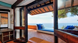 Ein Zimmer mit großem Fenster und Meerblick, eine Holzbank mit Kissen und eine rustikale Kommode.