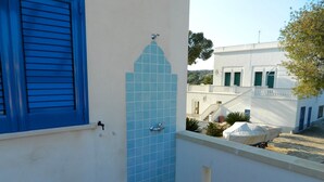 Un balcon avec un mur recouvert de carreaux bleus, une fenêtre avec des volets bleus et une vue sur un bâtiment blanc aux volets verts.
