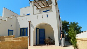 Un bâtiment moderne à la façade blanche, aux portes bleues et doté d’un espace extérieur abrité avec une pergola.