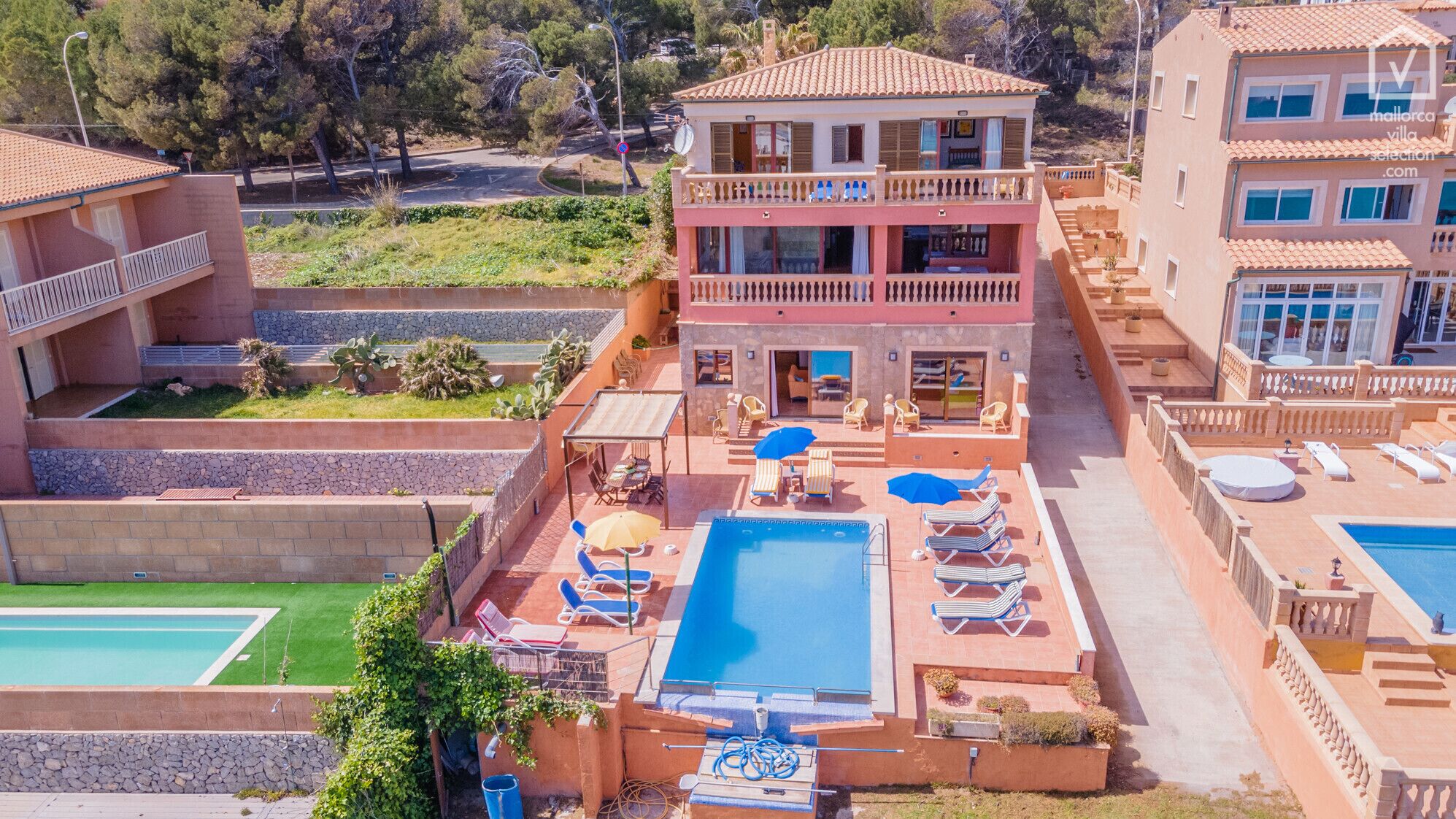 A two-story building with a pool, sun loungers, and a small garden area.