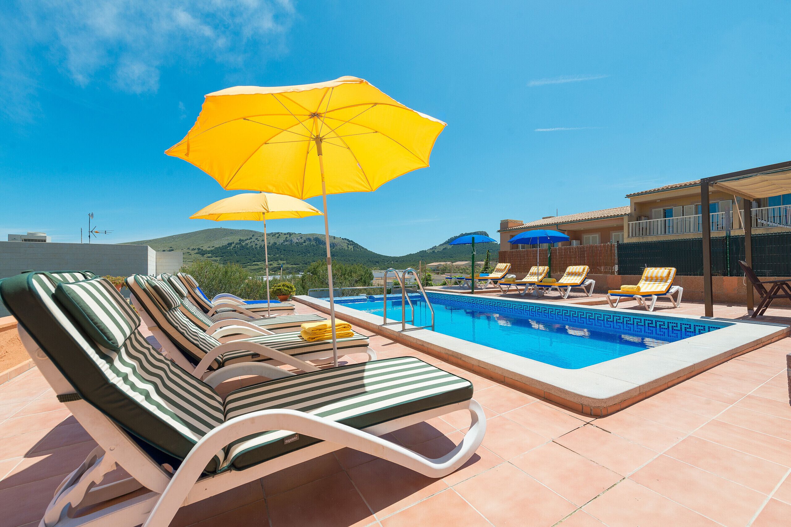 Zona junto a la piscina con sillones de descanso y sombrillas, una piscina y vistas a colinas al fondo.