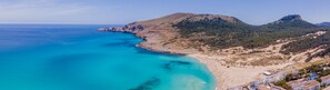 A coastal area with a beach, clear blue waters, and a mountainous backdrop.