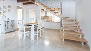 Eine großzügige Küche mit modernem Design, ein Essbereich mit Holztisch und weißen Stühlen sowie eine Treppe mit Holzstufen und Glasgeländern.