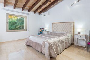Camera da letto con un letto grande, un comodino, una tavola di fianco al letto, una finestra vista verde, e un condizionatore d'aria.