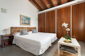Ein Schlafzimmer mit zwei Einzelbetten, einem Nachttisch, einer Nachttischlampe, einem gerahmten Gemälde an der Wand und einer Orchidee im Topf auf einem Beistelltisch.