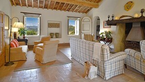 Ein gemütliches Wohnzimmer mit Kamin, einer Sofagarnitur und Blick ins Freie durch große Fenster.
