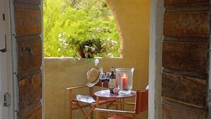 Ein holzrahmenfenster mit Blick auf Grünpflanzen und Blumen, ein kleiner Tisch mit Kerze, Weingläsern und einer Flasche.