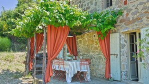 Ein Essbereich im Freien mit einem Steinhaus, roten Vorhängen und einem für eine Mahlzeit gedeckten Tisch.