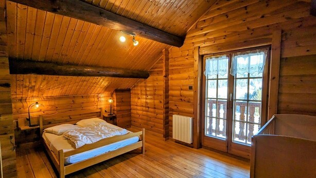 Un dormitorio rústico de cabaña de madera con una cama de madera, una mesita de noche, una ventana con cortinas y vistas al exterior.