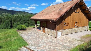 Una cabaña de madera con techo de tejas, cimientos de piedra y entrada pavimentada.