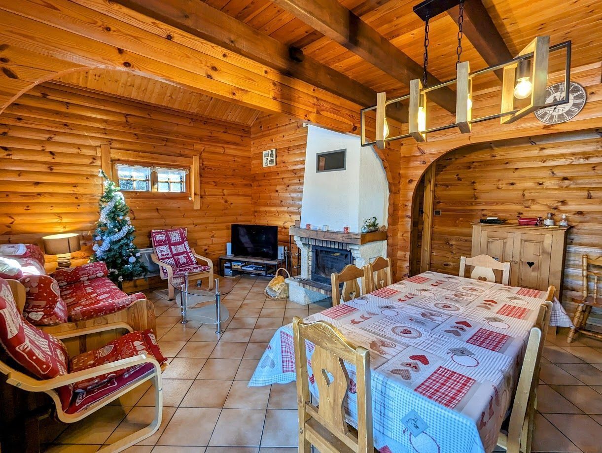 A cozy log cabin interior with a fireplace, a dining table, and a Christmas tree.