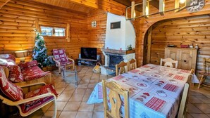 Un acogedor interior de cabaña de troncos con chimenea, una mesa de comedor y un árbol de Navidad.