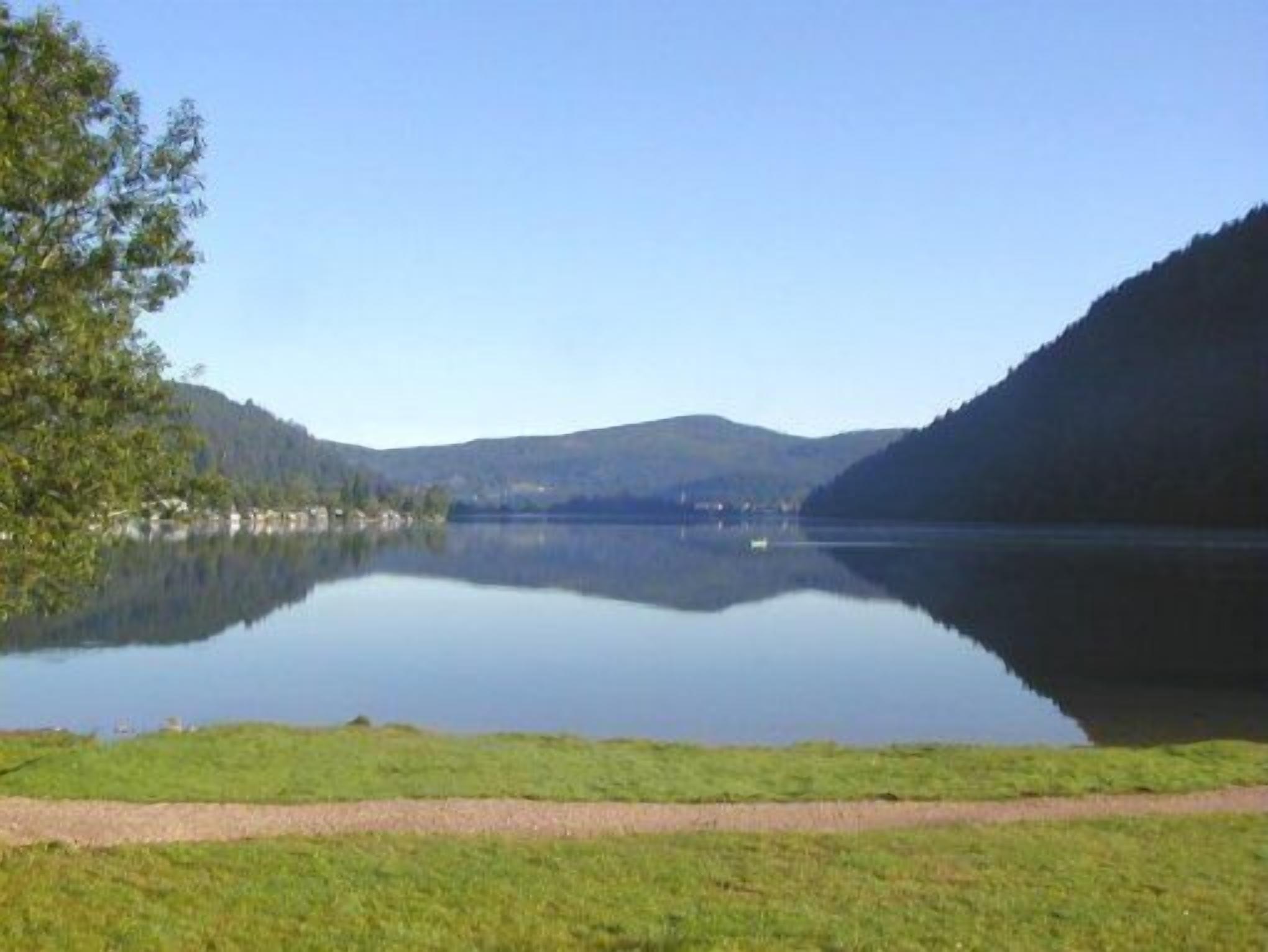 A tranquil lake with a clear view of the surrounding hills and a path leading to the water's edge.